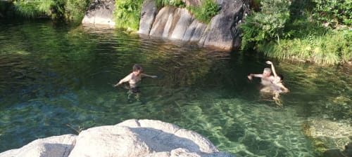 Huéspedes nadan en una piscina natural de color esmeralda en Aldea Rural Santo André, rodeada de rocas y exuberante vegetación en Ourense, España