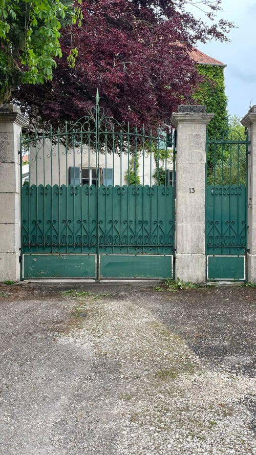 Portail en fer forgé vert orné à l'entrée de la Maison Agami à Rosières aux Salines, avec piliers en pierre d'époque et lierre