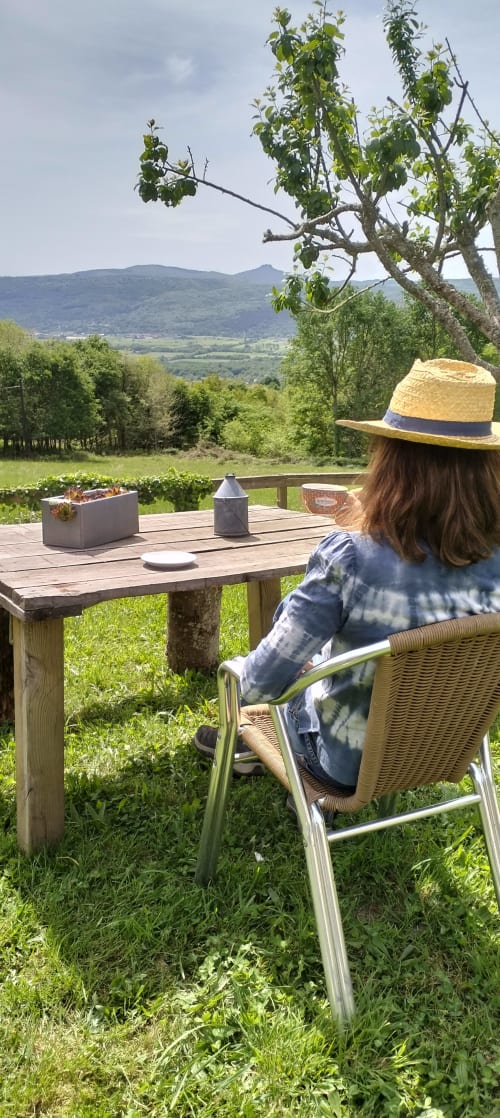 Mujer relajándose en Aldea Rural Santo André en Ourense, disfrutando de las vistas de verdes valles y montañas desde la terraza de madera