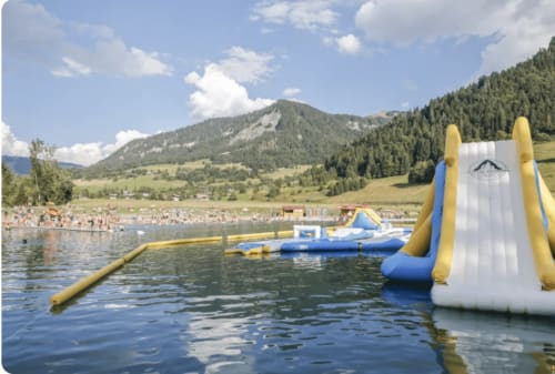 Inflatable water slides and floats on a lake with mountains and forest at Chez Francine, Flumet, France