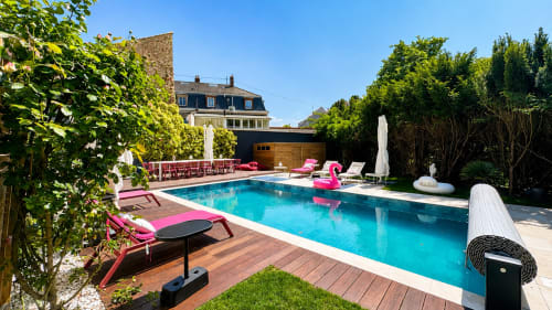 Piscine luxueuse de Villa Avril & Spa avec transats roses, eau turquoise et architecture de Sélestat en arrière-plan