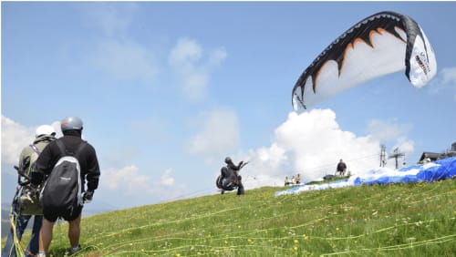 Paraglider preparing for flight at Flumet, French Alps with spectators watching on grassy hillside