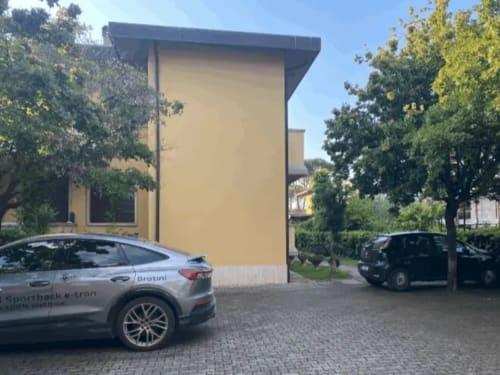 Edificio moderno giallo presso La Casetta dei Ronchi con auto elettriche parcheggiate e alberi circostanti