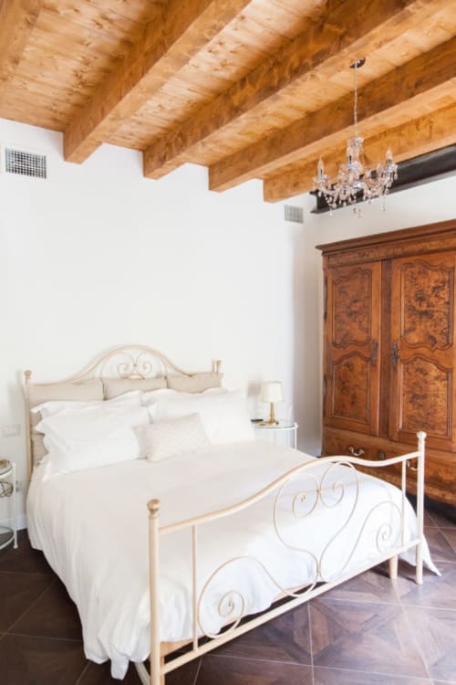 Elegant bedroom at Alessia's Place B&B in Como with exposed wooden beams, ornate bed, and antique armoire