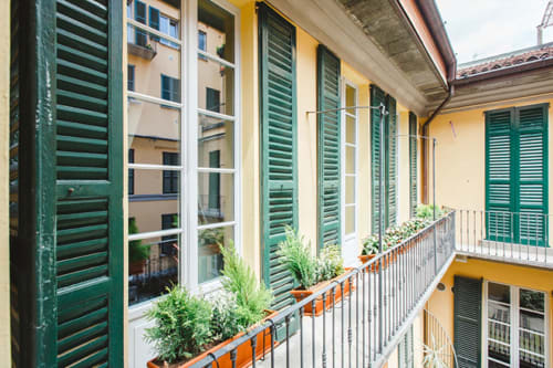 Alessia's Place balcony in Como with green shutters, potted plants, and yellow facade