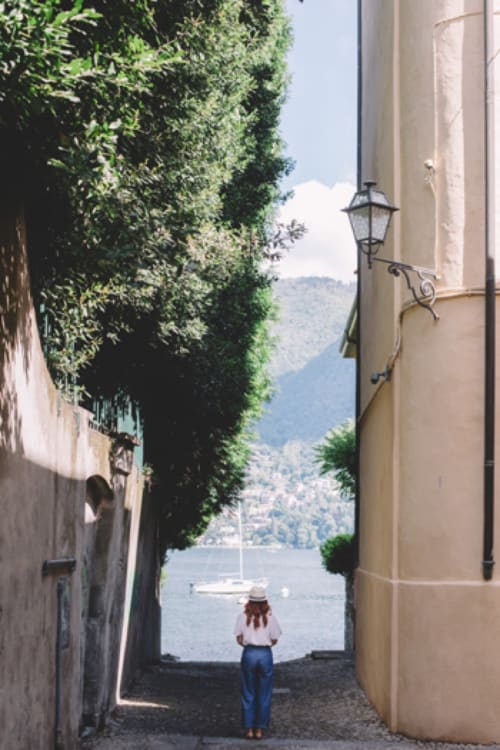 Donna in camicia bianca che ammira il Lago di Como da un vicolo coperto di edera, vela visibile, Alessia's Place BnB
