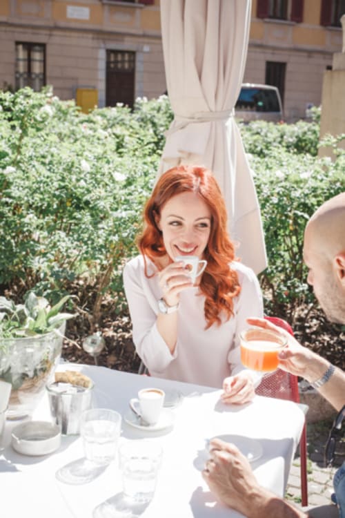 Donna con capelli rossi che gusta il caffè sulla terrazza di Alessia's Place a Como, circondata da fiori bianchi