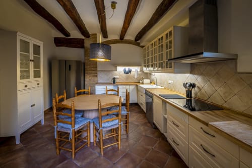 Cocina rústica de Ca L'Avi con vigas de madera, mesa de comedor, armarios blancos y electrodomésticos de acero inoxidable