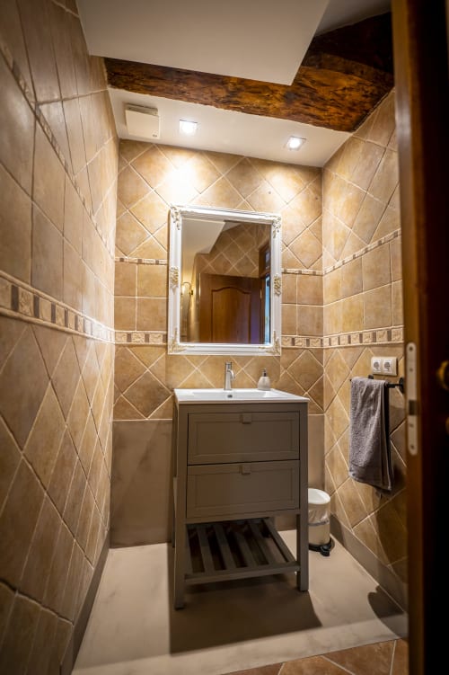 Elegante cuarto de baño en la casita Ca L'Avi con azulejos beige, espejo, lavamanos, toallero e iluminación de techo