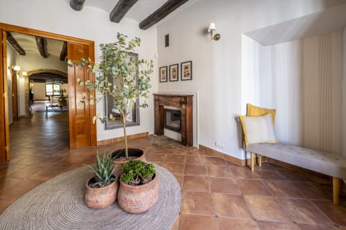 Sala de estar rústica con baldosas de terracota, vigas de madera, chimenea, plantas en maceta y asientos amarillos