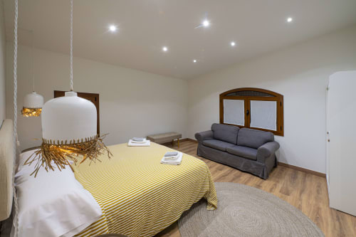 Amplio salón de la cabaña Ca L'Avi con cama de rayas amarillas, sofá oscuro, ventanas de madera e iluminación moderna