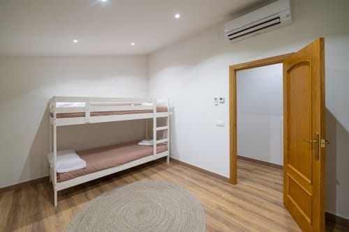 Dormitorio moderno con camas literas blancas, puerta de madera, pisos de madera y alfombra redonda en la casa rural Ca L'Avi