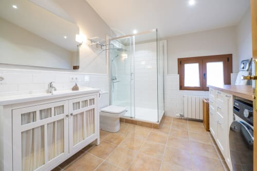 Baño moderno en el alojamiento rural Ca L'Avi de Estada Rural con ducha acristalada, tocador blanco y baldosas de terracota