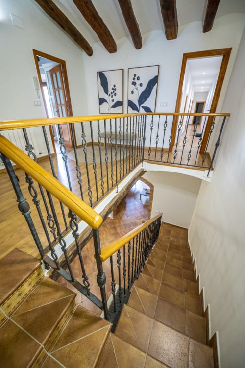 Escalera de madera con barandillas metálicas decorativas en la casa Ca L'Avi, vigas vistas, arte botánico enmarcado y espejos