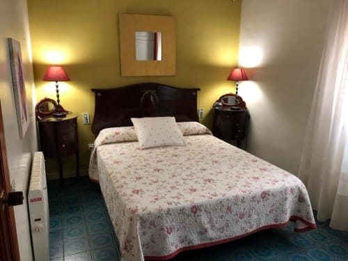 Habitación doble en el hotel Casa María de Artana con ropa de cama floral, cabecero de madera oscura, lámparas rojas y paredes con acento amarillo