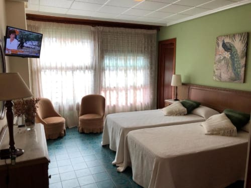 Luminosa habitación doble en Casa María con dos camas, paredes verdes, ventanas con vista a la montaña, TV y cómoda sala de estar