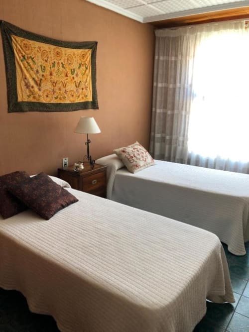 Dos camas dobles en habitación comunicante del hotel Casa María en Artana, con paredes de terracota, tapicería decorativa y vista a la montaña