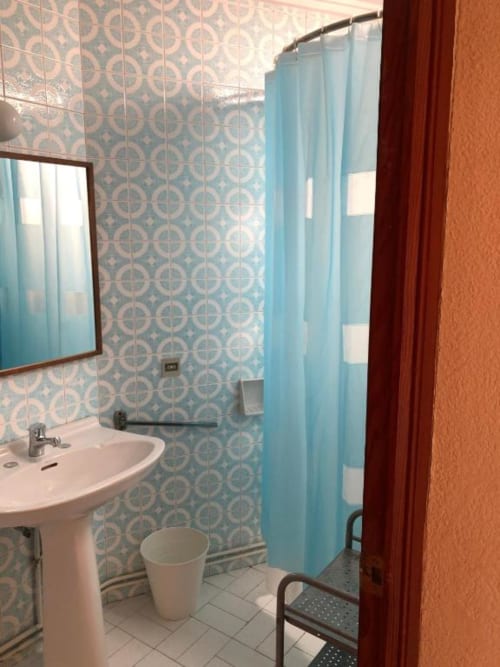 Baño del hotel Casa María en Artana con azulejos de patrón turquesa, lavamanos de pedestal, inodoro y cortina de ducha
