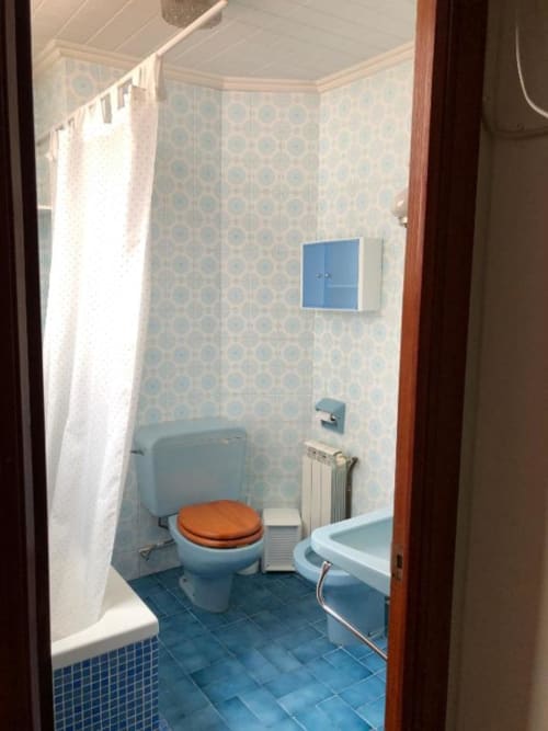Cuarto de baño luminoso en el hotel Casa María de Artana con inodoro azul, bañera y paredes con azulejos estampados