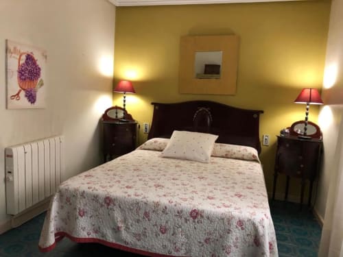 Acogedora habitación doble en Casa María con paredes amarillas, cabecero de madera oscura, ropa de cama floral, lámparas de noche y vistas a la montaña