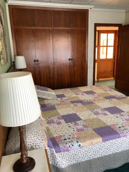 Amplio dormitorio doble en hotel Casa María, Artana, con colcha patchwork, armarios de madera, lámpara y puerta de entrada de madera.