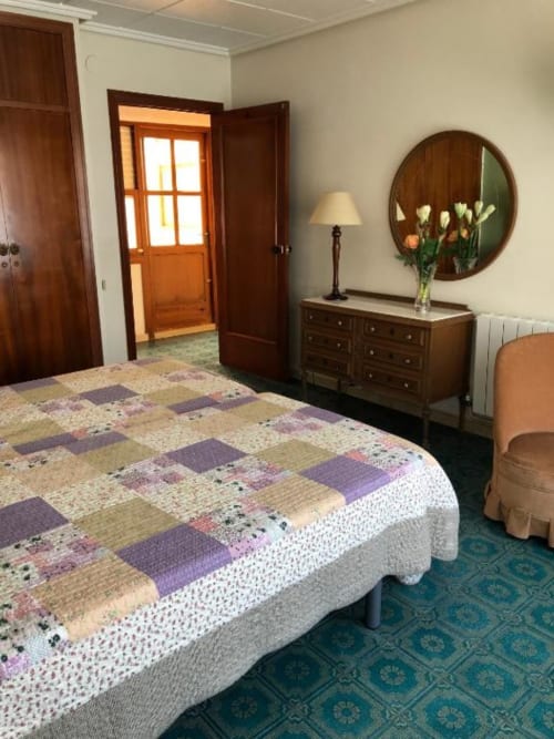Dormitorio doble Casa María en Artana con colcha patchwork, cómoda de madera, espejo redondo y puerta de entrada naranja