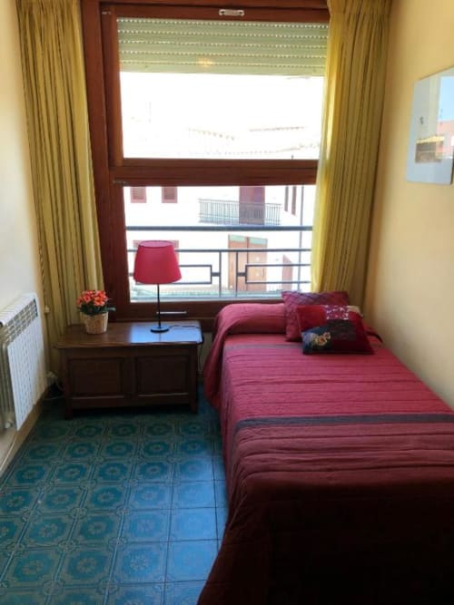 Pequeña habitación doble en el hotel Casa María de Artana con ropa de cama roja, escritorio de madera, balcón con vista a la montaña y cortinas color oliva.