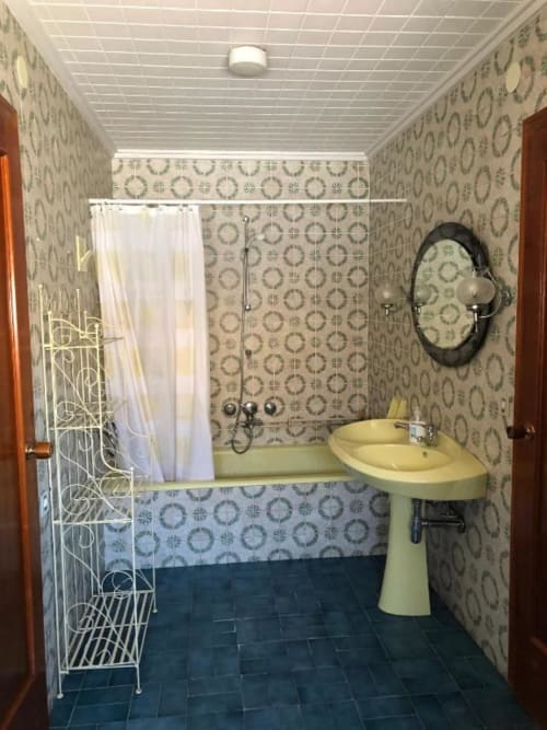 Baño con lavabo pedestal amarillo, bañera con cortina de ducha, azulejos decorativos en las paredes y espejo del hotel Casa María