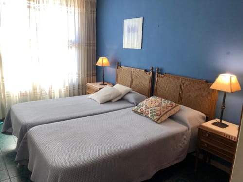 Dormitorio luminoso con dos camas dobles, paredes azules, cabeceros de mimbre y vistas a las montañas en el hotel Casa María de Artana, España