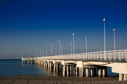 Moderno molo con ringhiere bianche e lampioni che si estende nel mare blu sotto un cielo terso