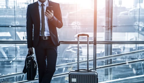 Uomo d'affari in abito con valigia e smartphone in moderno aeroporto con vista dello skyline cittadino, in viaggio verso La Casetta dei Ronchi