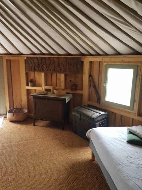 Intérieur douillet de yourte à La Toile Sous Les Etoiles à Charron : mobilier en bois, lit, kitchenette et plafond vitré