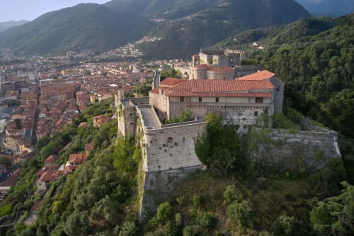 Castello medievale su collina che domina il borgo italiano tra verdi montagne e foreste