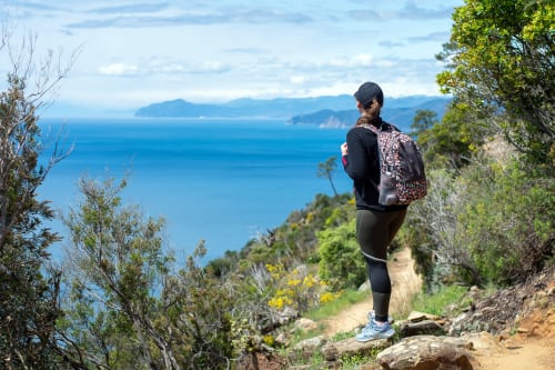 Escursionista con zaino su sentiero costiero con vista sul blu Mar Mediterraneo, Italia