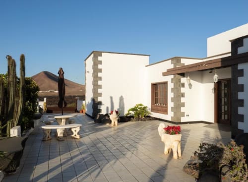 Villa Estrella Polar courtyard in Tahiche with white apartment building, terrace, cacti, and mountain views under clear blue