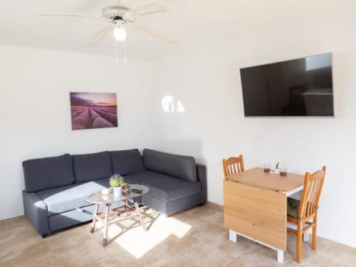 Modern living room in Villa Estrella Polar apartment with gray sofa, flat-screen TV, dining table, and natural light from
