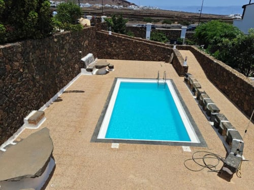 Rectangular swimming pool with bright blue water surrounded by sandy deck and stone walls at Villa Estrella Polar in Tahiche