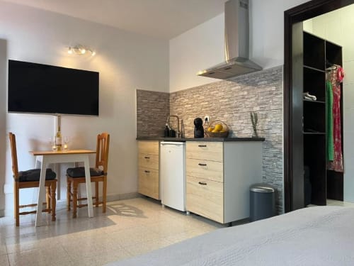 Modern kitchenette with wooden cabinets, dining area, and flat-screen TV at Villa Estrella Polar apartment in Tahiche
