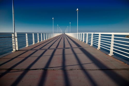 Lungo molo in legno con ringhiere bianche che si estende nel mare blu calmo sotto un cielo limpido