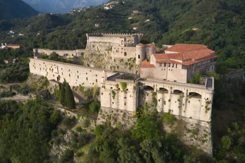 Castello medievale arroccato su una collina rocciosa circondato da rigogliosa foresta verde in Italia