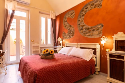 Bright bedroom at Casa Scola Loano with red bedspread, white pillows, orange accent wall, and terrace doors in Loano, Italy