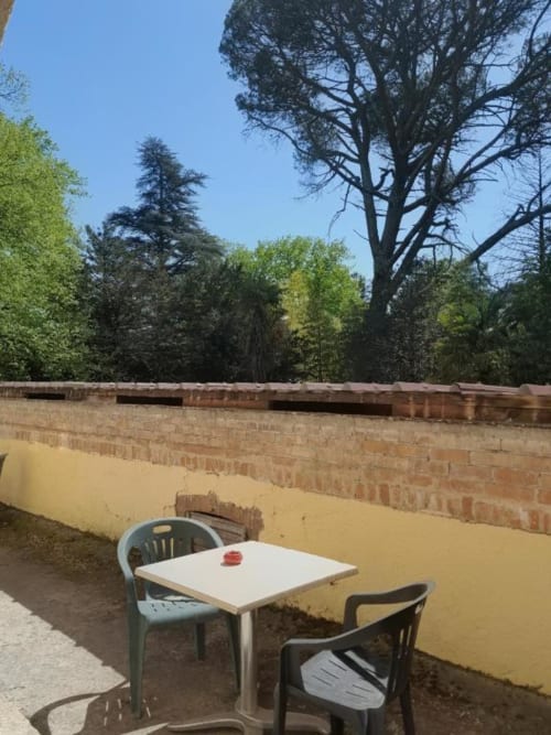 Terrace at Domaine de Cabrières with dining table and chairs overlooking gardens and trees, St Jean Du Gard