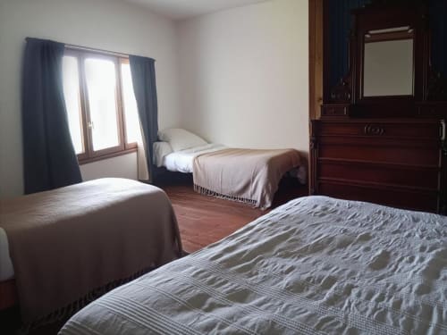 Spacious quadruple bedroom at Domaine de Cabrières with three beds, wooden dresser, and blue curtains at St Jean Du Gard.