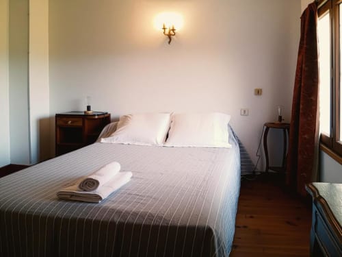 Spacious double bedroom at Domaine de Cabrières with striped bedding, white pillows, wooden nightstands, and warm wall sconce