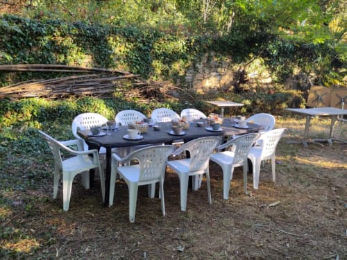 Outdoor dining setup at Domaine de Cabrières with white chairs and black table in garden surrounded by greenery.