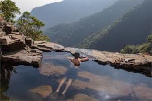 Huésped relajándose en piscina natural de roca con vistas a las montañas en Aldea Rural Santo André, Ourense