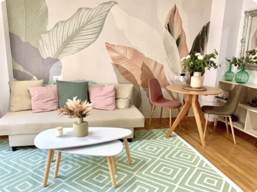 Moderno salón de apartamento en Málaga con sofá crema, cojines rosa, mesa de centro redonda, alfombra geométrica y decoración botánica