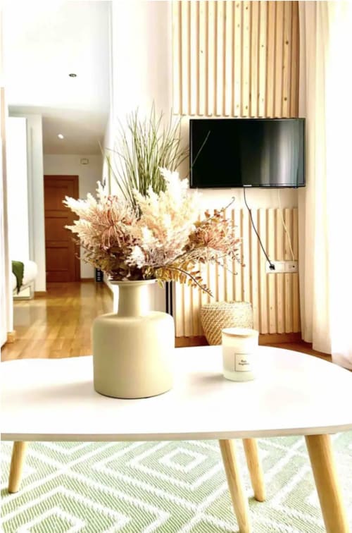 Elegante sala de estar moderna en Málaga con jarrón blanco de flores secas, TV de pared, mesa de madera y decoración