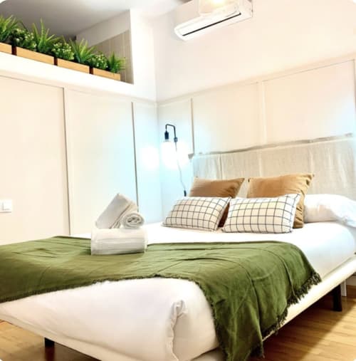 Dormitorio moderno en apartamento de Málaga Centro con ropa de cama verde, cabecero blanco, cojines decorativos, plantas en maceta y elementos de madera