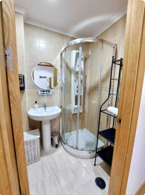 Baño moderno en apartamento de Málaga con ducha, lavabo pedestal, espejo redondo y toallero negro